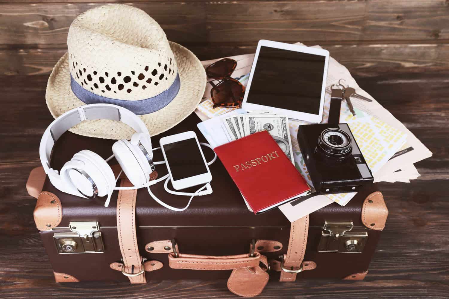 Travel essentials including hat, passport, camera, and gadgets on a suitcase.