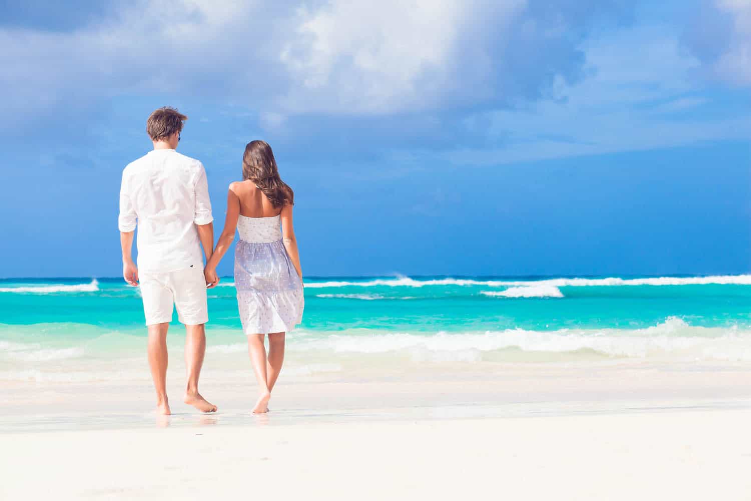 Romantic couple walking hand in hand on tropical beach.