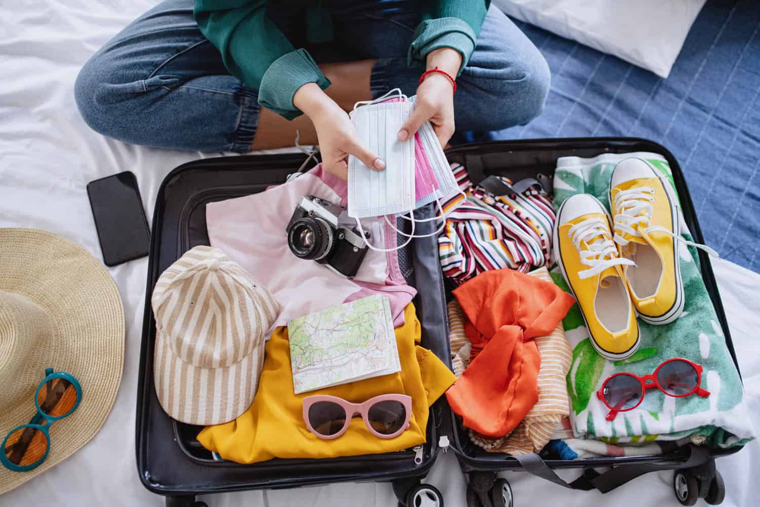 Open suitcase with travel essentials including shoes, sunglasses, camera, and clothes.